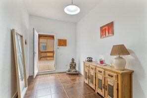 Een gang met een houten kast, een beeld en een deur naar een kamer.