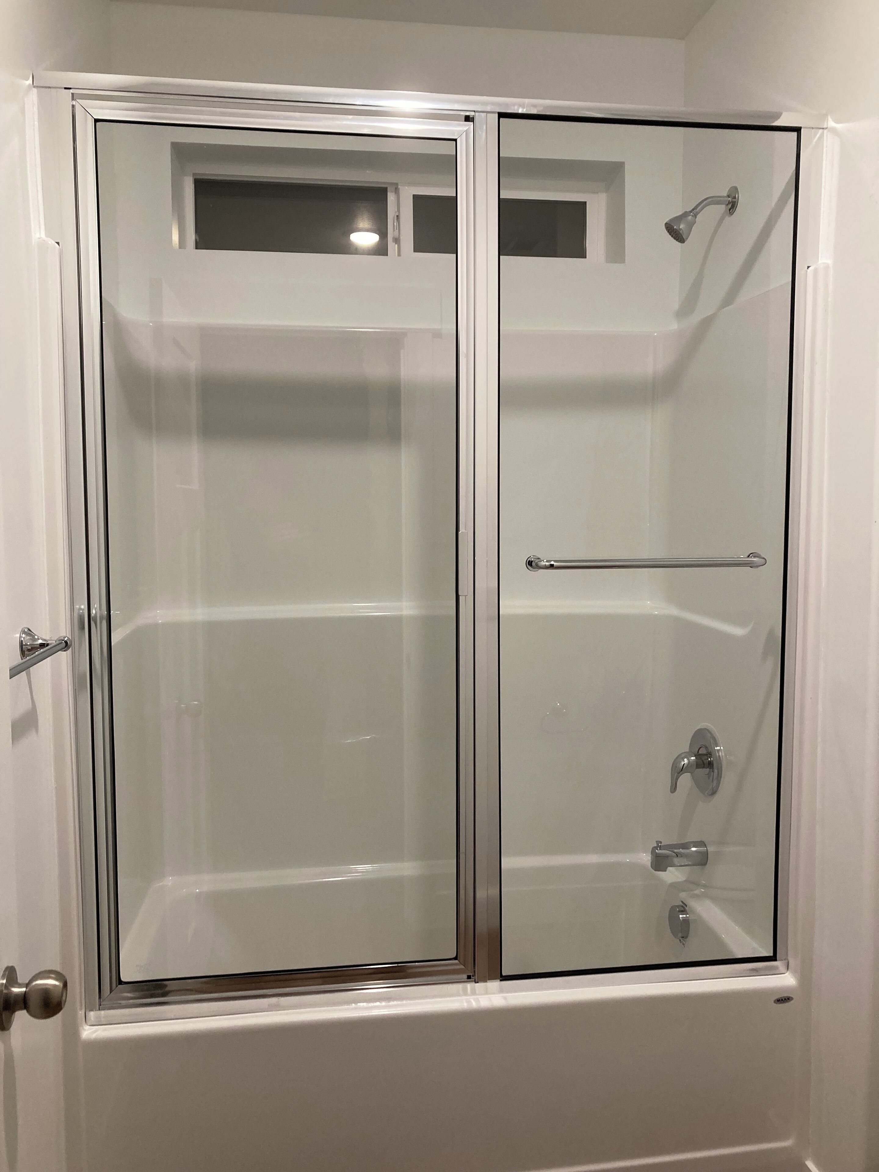 A glass-enclosed shower stall with a door, a towel bar, and a showerhead.