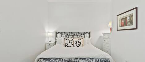Een slaapkamer met een bed, nachtkastje, dressoir, plafondventilator en een lijst met een afbeelding aan de muur.