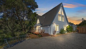 A two-story house with a steeply pitched roof, a front porch with a railing, and a gravel driveway. - Riverfront Escape in North Alexander Vly, 3BR/2BA, hot tub, bbq, bocce ball (Cloverdale)