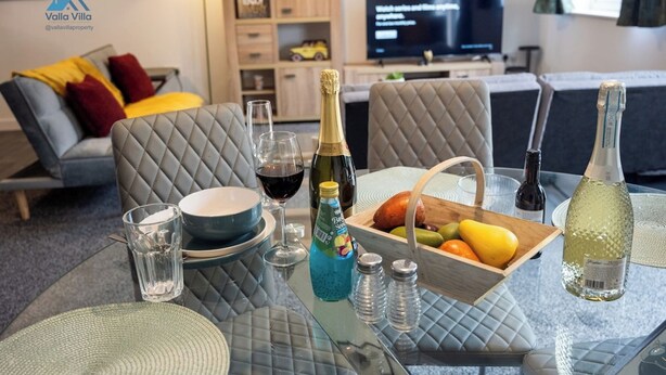 Sala de estar con una mesa de vidrio dispuesta para comer, un sofá, un televisor mostrando Netflix y un aparador de madera al fondo.