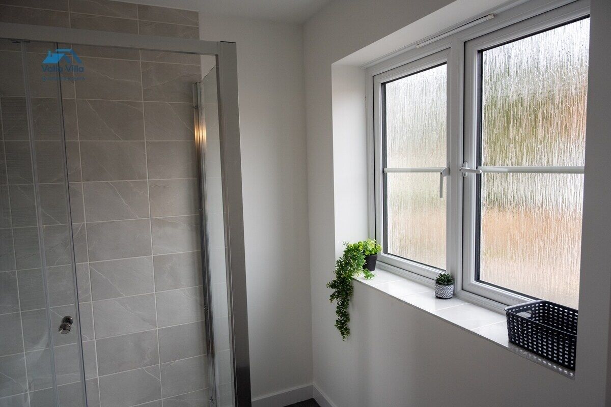 A bathroom with a glass shower enclosure, a window with a view, and a potted plant on the windowsill.