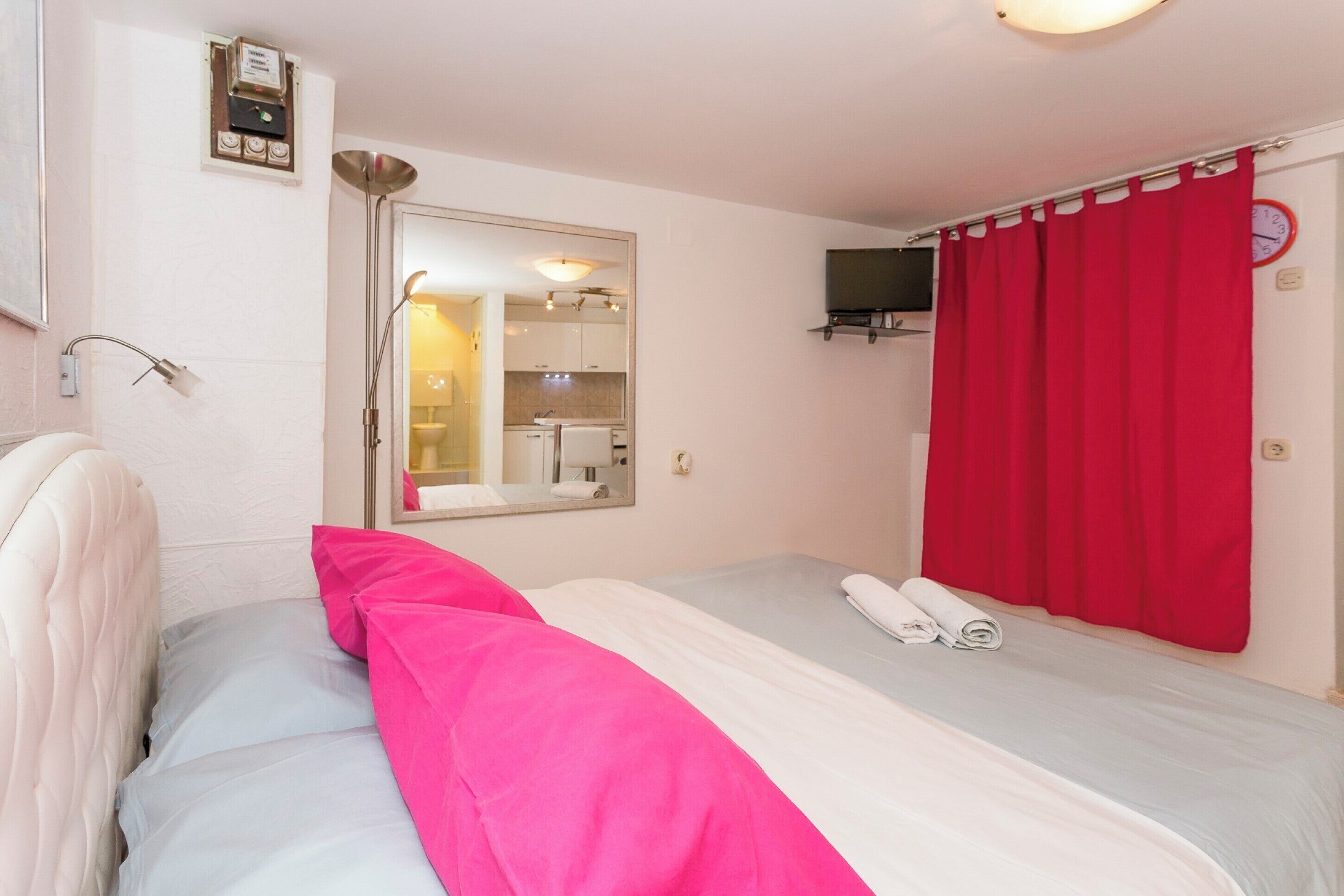 A hotel room with a bed, a mirror, a TV, and a red curtain.