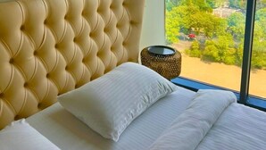 Une chambre dotée d’une grande fenêtre, d’une tête de lit capitonnée et de trois tableaux accrochés au mur.