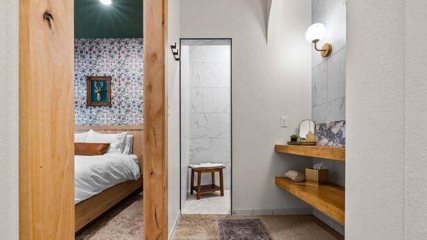 Une chambre à coucher avec un lit en bois, un petit tabouret et une salle de bain avec un mur en marbre et des étagères en bois.