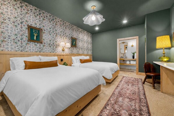Habitación de hotel con dos camas, cabecera de madera, alfombra estampada, escritorio con lámpara y un espejo.