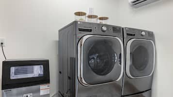 A laundry area with two front-loading LG washers, a VEVOR refrigerator, and an air conditioning unit on the wall.