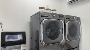 A laundry area with two front-loading LG washers, a VEVOR refrigerator, and an air conditioning unit on the wall.