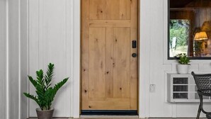 Une porte en bois surmontée d’un luminaire noir, un pot de fleurs à gauche et une chaise à droite.