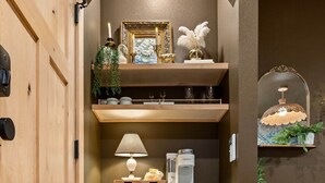 Un espace cuisine compact comprenant un petit réfrigérateur, des étagères ornées d’objets décoratifs et un luminaire suspendu.