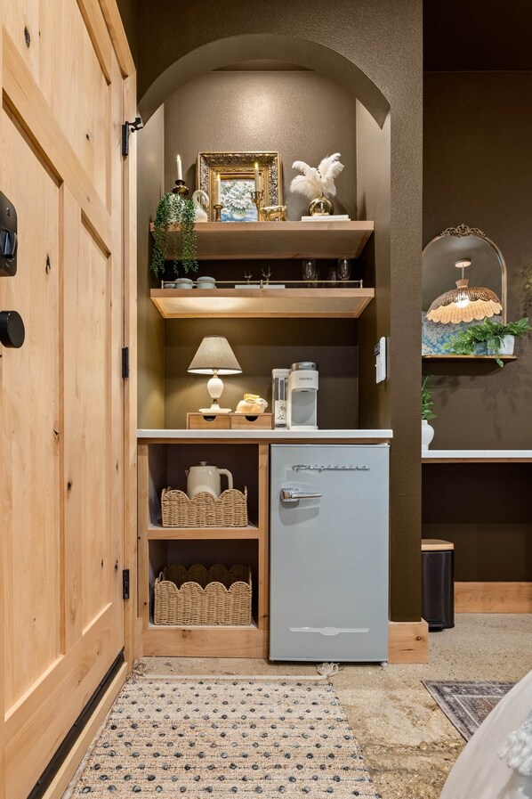 Un espace cuisine compact comprenant un petit réfrigérateur, des étagères ornées d’objets décoratifs et un luminaire suspendu.