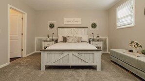 A bedroom with a bed, two bedside tables, a nightstand, a bench, and a window with blinds. - First Floor Getaway in Meadville (West Mead Township)
