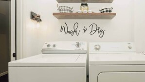 A laundry area with two white washers and dryers, a shelf with jars and a 'Wash & Dry' sign, and a wall-mounted light fixture. - First Floor Getaway in Meadville (West Mead Township)