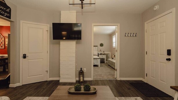 A hallway with a flat-screen TV mounted on the wall, a white brick accent wall, and a wooden table with a tray of small plants. - First Floor Getaway in Meadville (West Mead Township)