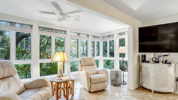 A spacious living room with a large window, a ceiling fan, a sofa, a recliner, a coffee table, and a TV. - Charming condo with private beach access, on-site golf, high-speed WiFi & AC (Kiawah Island)