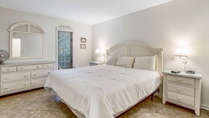 A bedroom with a bed, nightstands, a dresser, a mirror, and a window with blinds. - Charming condo with private beach access, on-site golf, high-speed WiFi & AC (Kiawah Island)