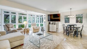 A spacious living room with a glass coffee table, beige sofa, and a dining area with a table and chairs. - Charming condo with private beach access, on-site golf, high-speed WiFi & AC (Kiawah Island)