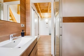 Une salle de bain moderne avec un grand miroir, un lavabo blanc, un lambris en bois et un plafond en bois.