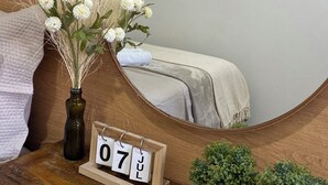 A wooden bedside table with a mirror, a vase of white flowers, a small wooden calendar, and two potted plants. - Hostel Amor por SP  (São Paulo)