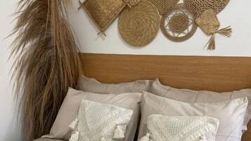 A bed with beige bedding, two decorative pillows, and a rolled towel with a lavender flower.