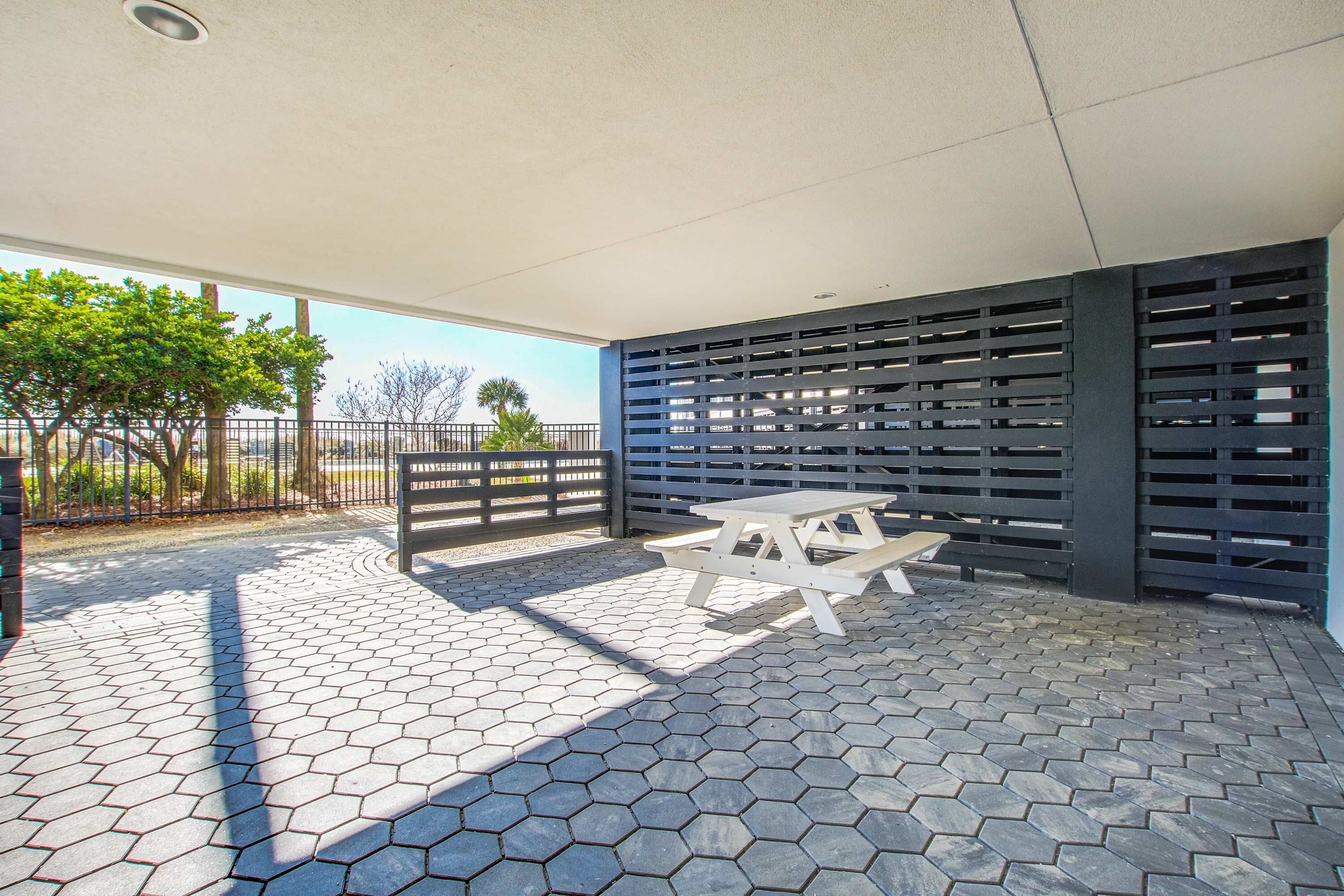 Un patio couvert doté d’un sol carrelé en forme d’hexagone, d’une table de pique-nique blanche et d’une clôture noire avec un portail.