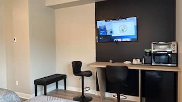 Una habitación de hotel moderna con una cama, un escritorio con una computadora, una cafetera y dos taburetes de bar.