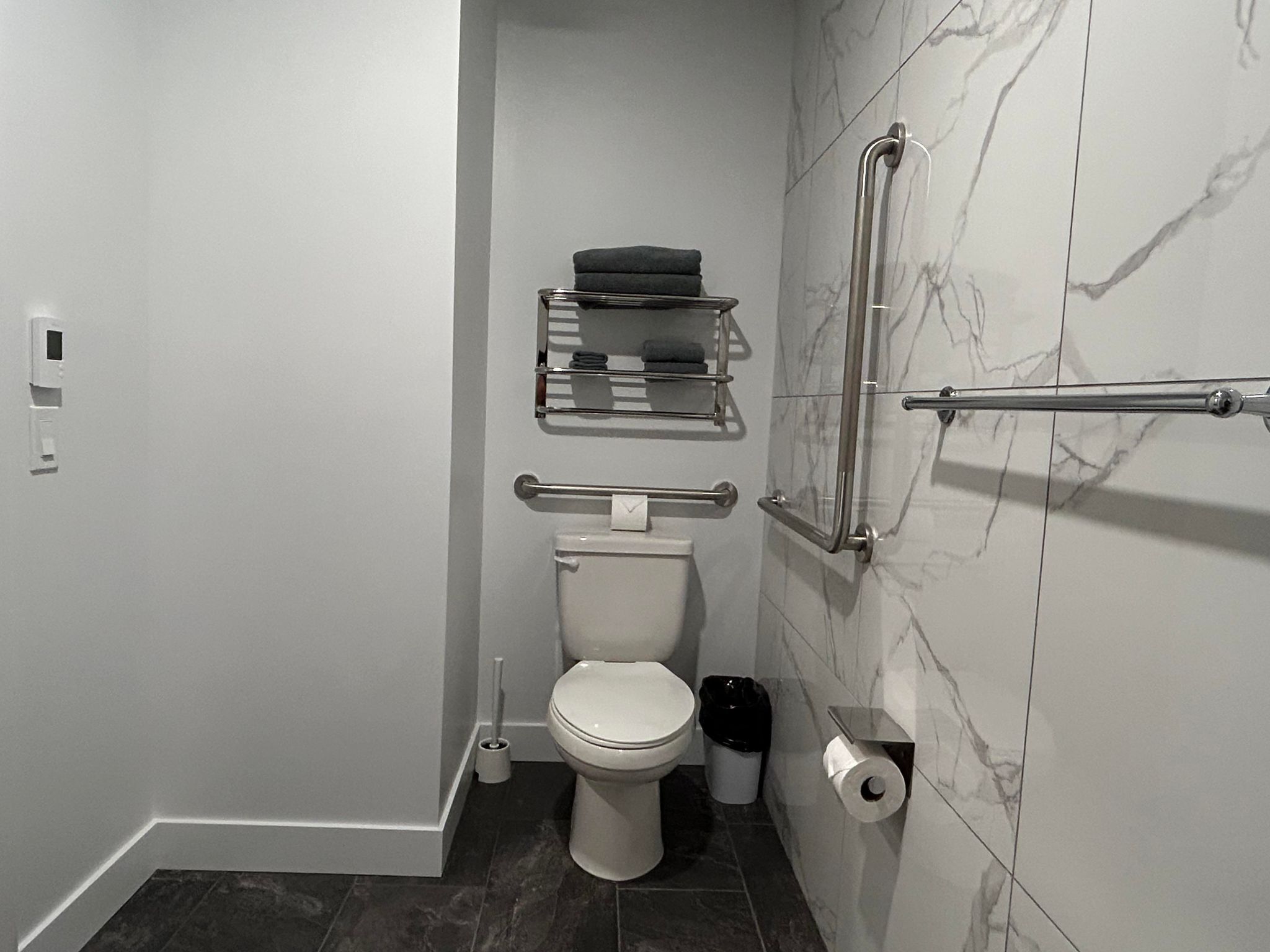 Um banheiro moderno com vaso sanitário, secador de mãos, lixeira e porta-toalhas.