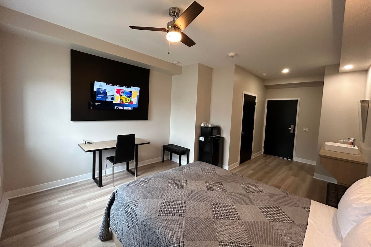 Une chambre d’hôtel moderne dotée d’un grand lit, d’un bureau avec une chaise, d’un téléviseur fixé au mur et d’un ventilateur de plafond.