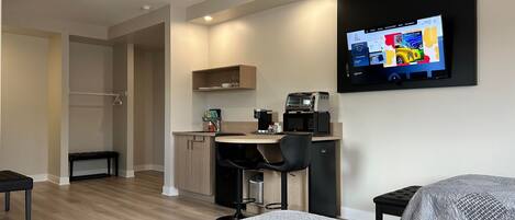 A compact hotel room with a kitchenette, a bed, a TV, and a small seating area.