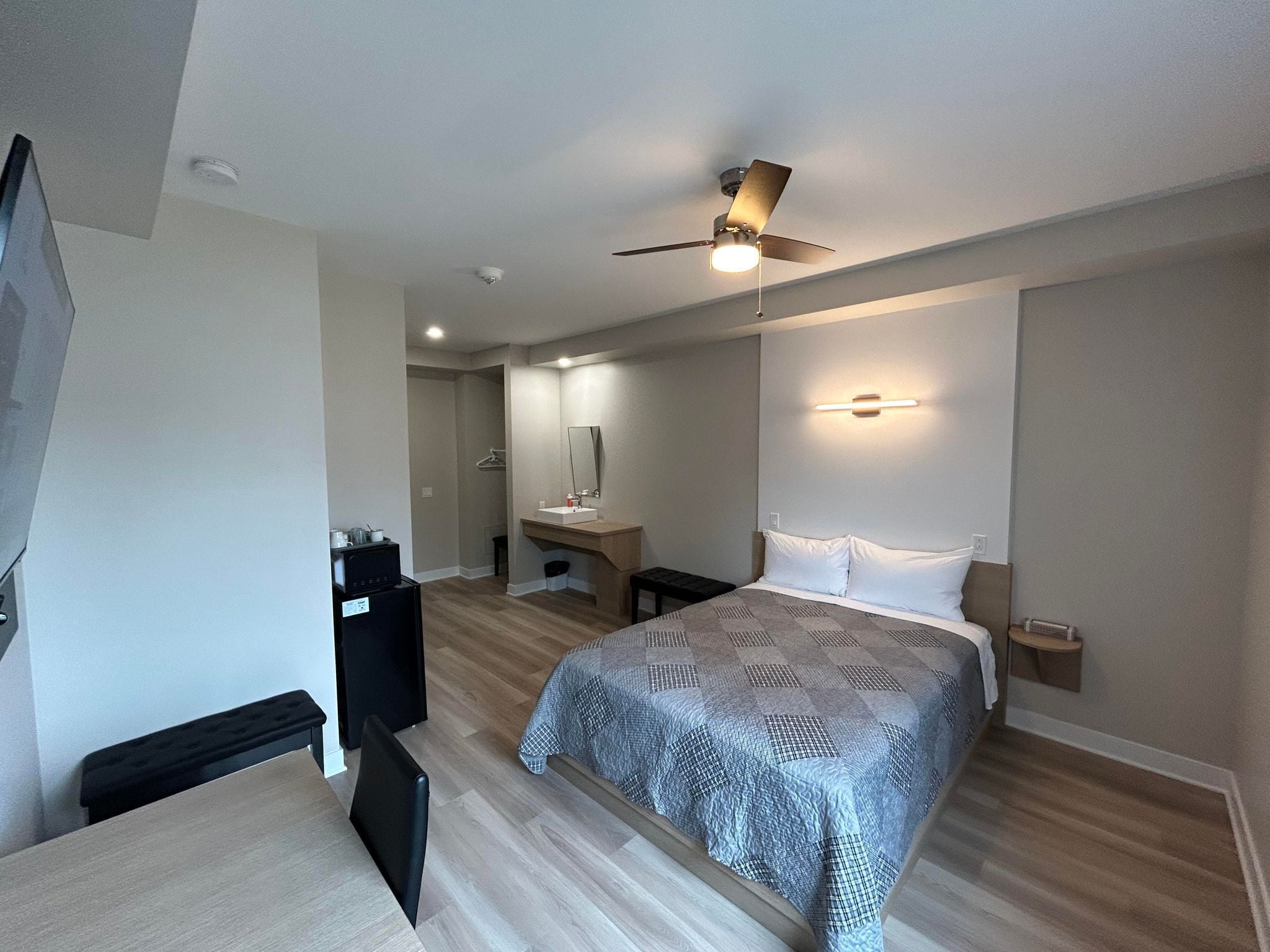 A modern hotel room with a large bed, a desk, a chair, a wardrobe, a mirror, and a ceiling fan.