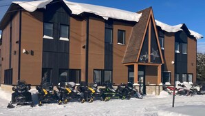 A modern building with a brown facade and large windows, surrounded by snow. - Hôtel St-Michel (Saint-Michel-des-Saints)