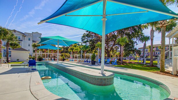 A swimming pool with blue umbrellas, lounge chairs, and palm trees. - Stylish 2BR: Pet Friendly in Walkable Resort with a Pool (Charleston)