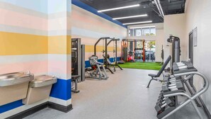 A gym with various exercise equipment, a wall with a colorful stripe pattern, and a window with a view of the outdoors. - Stylish 2BR: Pet Friendly in Walkable Resort with a Pool (Charleston)