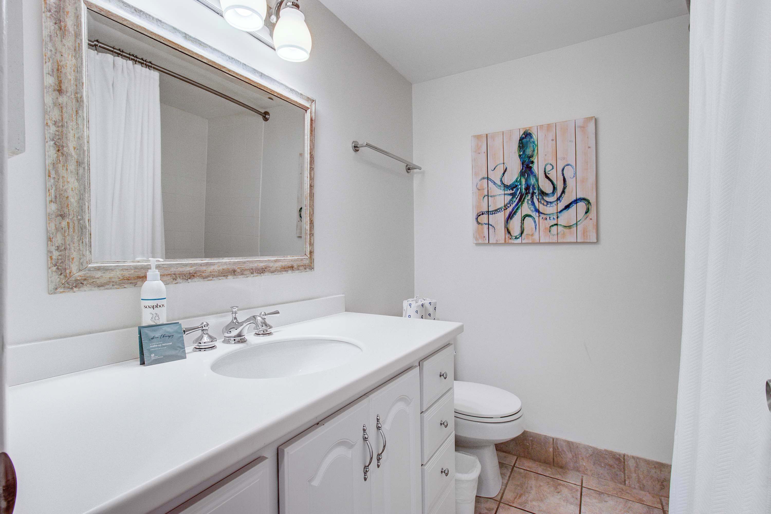 A bathroom with a white sink, a mirror with a rustic frame, a toilet, and a wall-mounted painting of an octopus.