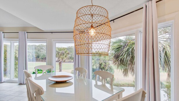 A dining area with a glass table, white chairs, and a woven pendant light.