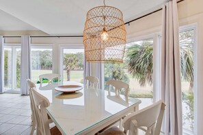 Un espace repas avec une table en verre, des chaises blanches et un luminaire suspendu en fibres tressées.