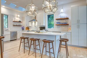 A modern kitchen with a central island, bar stools, pendant lights, and a view of greenery outside. - Lovely Estate w/ Private Pool in Wild Dunes Resort - Walk 1 Block to Beach (Isle of Palms)