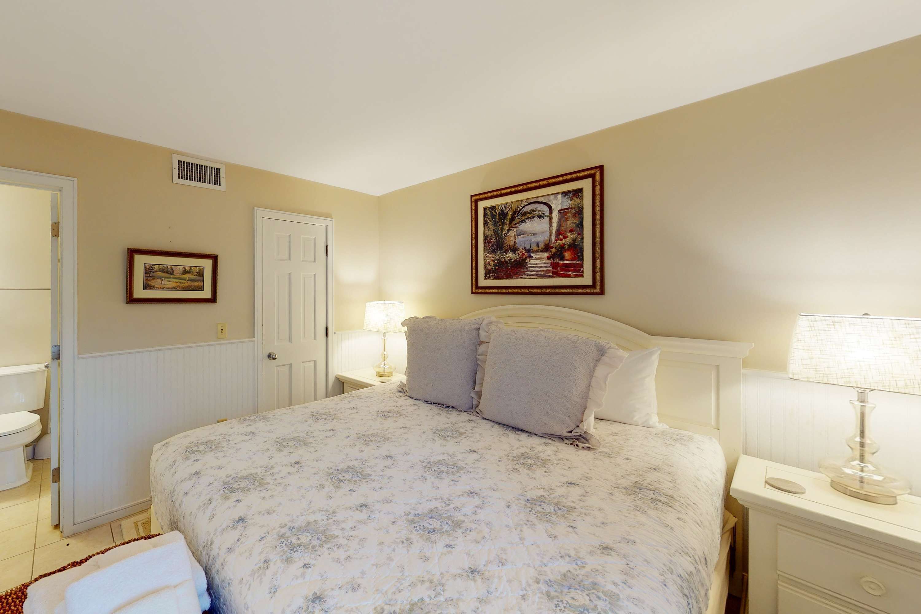 A bedroom with a bed, bedside tables, a nightstand, a door, and a framed picture on the wall.