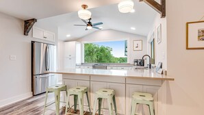 A kitchen with a large island, bar stools, a refrigerator, and a ceiling fan. - Fantastic coastal retreat with private dock, gas grill, two decks, & fast WiFi (Folly Beach)