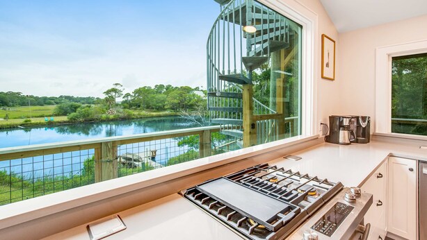 A kitchen with a view of a lake, a spiral staircase, and a coffee maker. - Fantastic coastal retreat with private dock, gas grill, two decks, & fast WiFi (Folly Beach)
