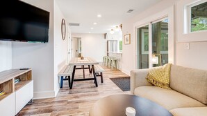 A modern living room with a large flat-screen TV, a wooden coffee table, and a beige sofa with a throw blanket. - Fantastic coastal retreat with private dock, gas grill, two decks, & fast WiFi (Folly Beach)