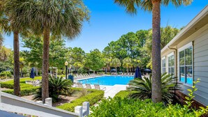 A pool area with lounge chairs and umbrellas, surrounded by palm trees and well-maintained landscaping.