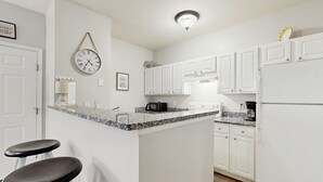 A kitchen with white cabinets, a granite countertop, a clock, and a coffee maker.