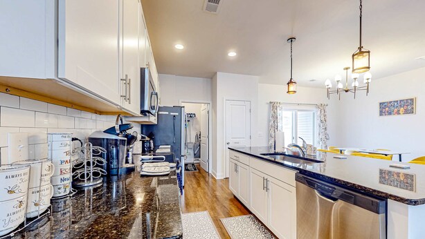 A modern kitchen with white cabinets, a stainless steel dishwasher, and a granite countertop. - Snowbird-friendly townhouse with pool, tennis court, & central AC (North Charleston)