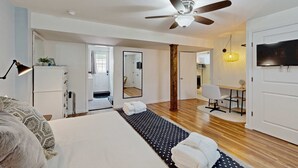 Una habitación de hotel moderna con una cama grande, un ventilador de techo, un televisor y un comedor con mesa y sillas.