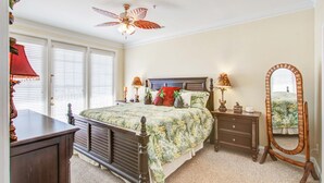 Une chambre à coucher comprenant un lit, une commode, des tables de chevet, un ventilateur de plafond et un grand miroir.