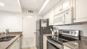 Cozinha moderna com armários brancos, eletrodomésticos de aço inoxidável e bancadas de granito.