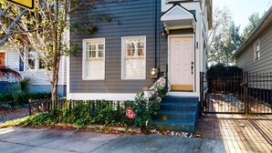 A two-story residential building with a gray exterior, white trim, and a front door with a small porch. - North Central, 30-Day Rental Home w/Double Porches, Garden Patio, and Free WiFi (Charleston)