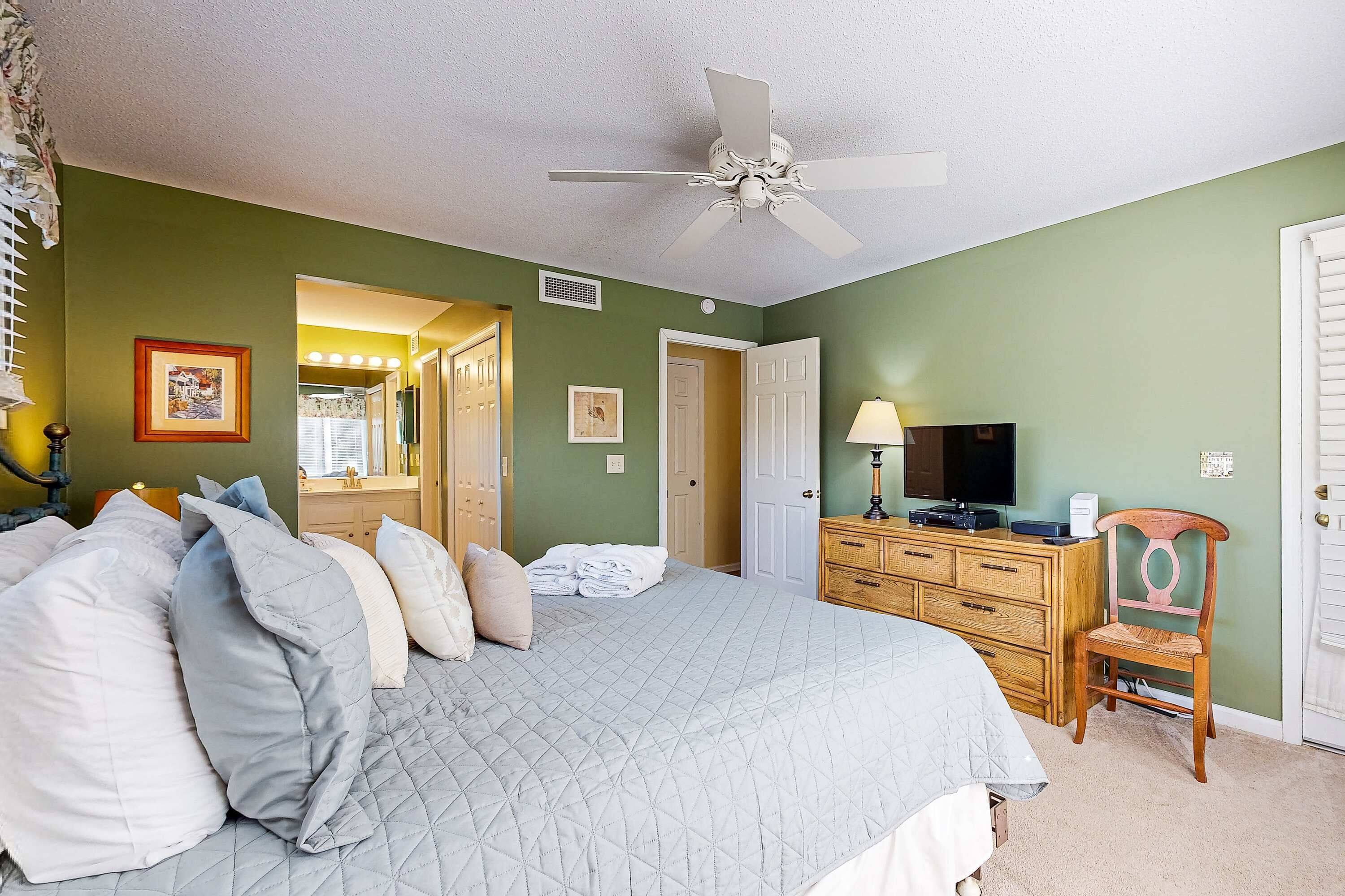 A bedroom with a bed, a wooden dresser, a television, and a ceiling fan.