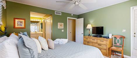 A bedroom with a bed, a wooden dresser, a television, and a ceiling fan.